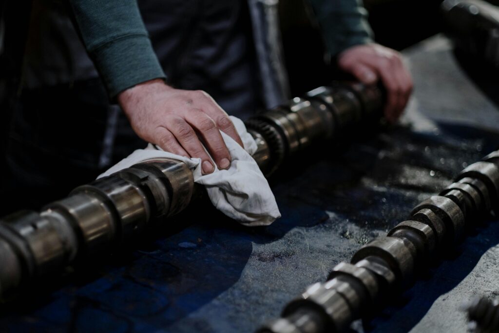 Close-up of a mechanic cleaning a camshaft with a cloth in an industrial setting.
